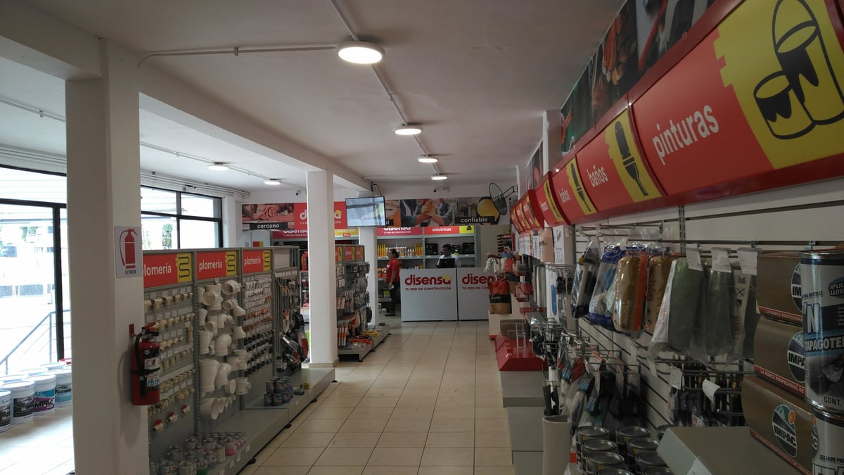 Interior de tienda comercial con estanterías exhibiendo productos, señalización publicitaria en rojo, letrero de Disensa y piso de loseta